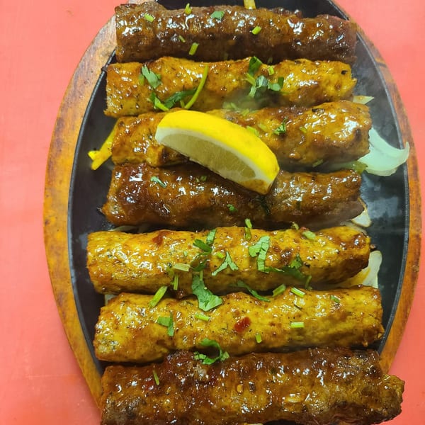 Indian seekh kebabs, some dark brown and some golden, garnished with cilantro and a lemon wedge.