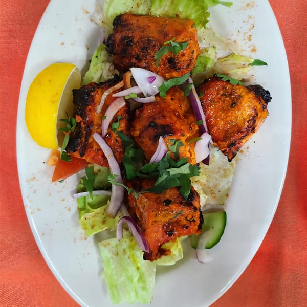 Indian chicken tikka with red onions, cilantro, lemon, and lettuce on a white plate.
