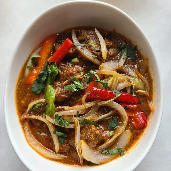 Indian curry with red and green peppers, onions, and cilantro in a white bowl.